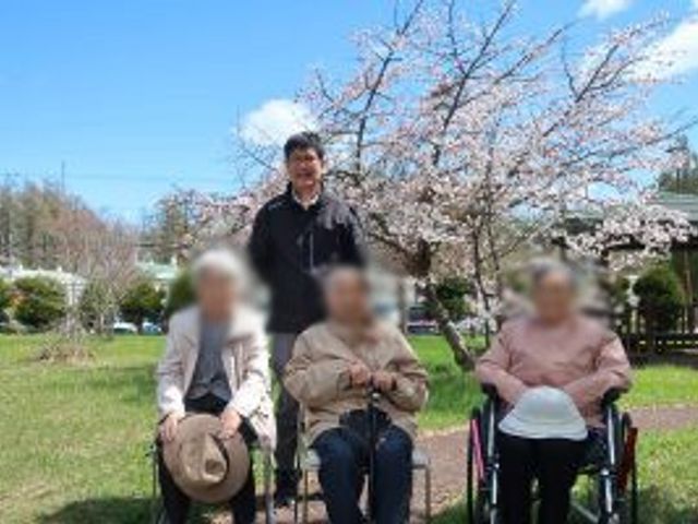 桜の木が見える庭 庭 スタッフと利用者が桜の木の下で和やかに過ごす様子です。自然を感じられる快適な空間です。