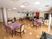 サムネイル 施設の写真 奥行きがあり、開放的な食堂である。薄紫のテーブルクロスにビニールカバーを掛けたテーブルと、椅子が配置されている。