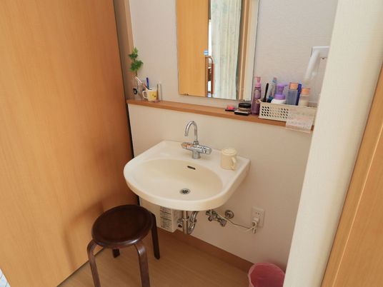 施設の写真 居室の一角に洗面スペースを設けている。上部の壁には鏡と小物棚を設置し、洗面ボウルの下には空間を確保している。