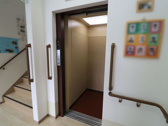 手すり付き階段とエレベーター エレベーター 手すりが設置された階段の横に、エレベーターの扉が開いており、どなたでも安全に移動できる環境が整っています。
