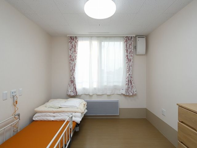 ベッドと窓がある室内 居室 広々とした居室で、自然光が入る明るいスペースです。快適な環境で過ごせます。