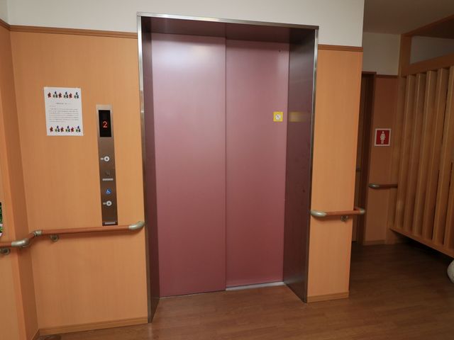 木目調エレベーター前 エレベータ― 手すり付きエレベーター前は、広々としており、利用者の移動がしやすい設計です。ゆとりを持ってご利用いただける環境が整っています。