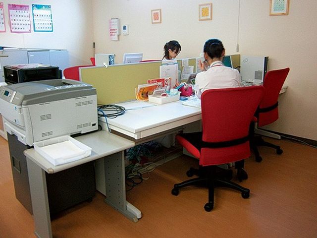 事務机のある内観 内観   受付周りに机が並ぶ落ち着いた空間です。赤い椅子に座って作業する様子が見え、事務のしやすさが伝わります。