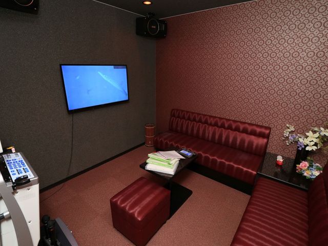 赤いソファのある部屋 カラオケルーム 落ち着いた雰囲気の娯楽室で、大型画面での映画鑑賞やカラオケをお楽しみいただけます。皆で集まり、楽しい時間を過ごす空間です。