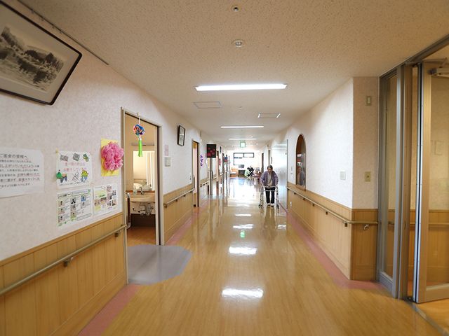 明るい長い廊下 廊下 木目調の温かみある廊下で、手すりが設置され安全に配慮されています。奥には自然光が差し込みます。