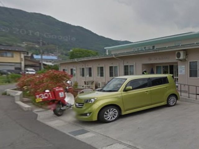 外観の建物と車両 エントランス 建物の入口には明るい色の車が停められ、訪れる人々を歓迎しています。周辺環境も広く、安心感のある佇まいです。