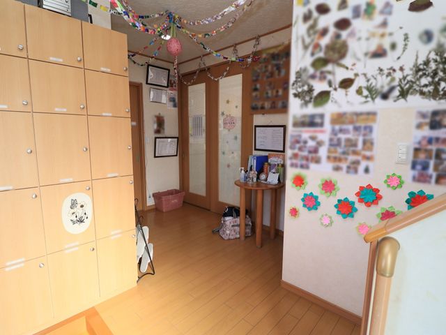 廊下のアクセント装飾 玄関 温かみのある廊下には、色とりどりの飾りがあり、壁には明るい雰囲気を醸し出す掲示物が配置されています。手すりに沿って歩行のサポートも考えられた空間です。