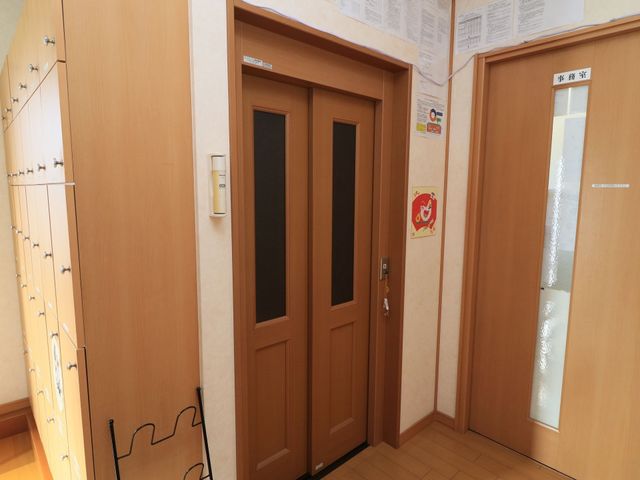廊下と部屋のドア エレベーター 木目調の温かみのある廊下が、訪れる皆様を穏やかに迎え入れます。明るく清潔感のある環境でお仕事ができる空間です。