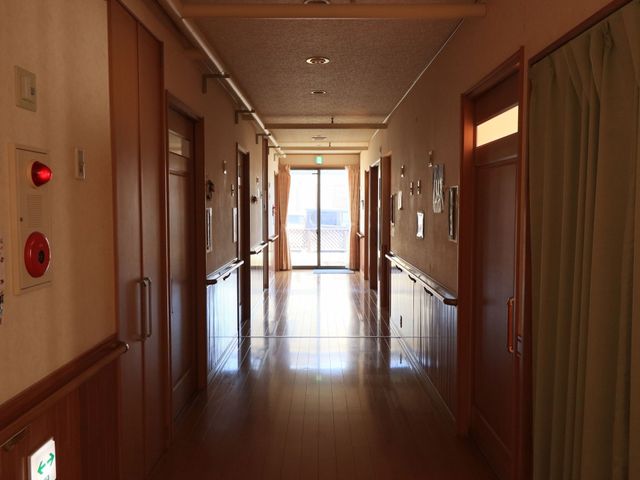 温かみのある廊下 通路 手すりが設置された落ち着いた色合いの廊下は、安心して歩ける配慮がされています。窓から自然光が差し込み、開放的な雰囲気を感じられます。