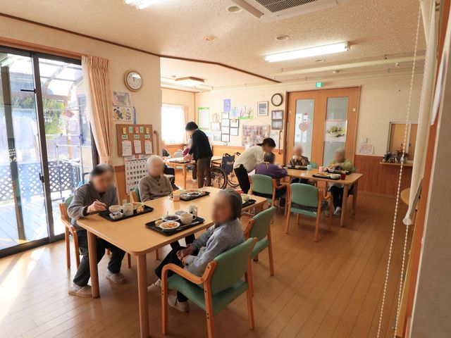 明るい食堂の様子 食堂 ゆったりとしたテーブルで食事を楽しむ方々が見られ、スタッフの方が丁寧に対応しています。温かみのある環境で、のびのびと過ごせそうですね。