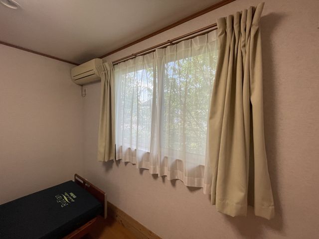 カーテンとベッドの居室 居室 明るい自然光が差し込む、快適な居住空間です。エアコンも完備され、快適に過ごせます。