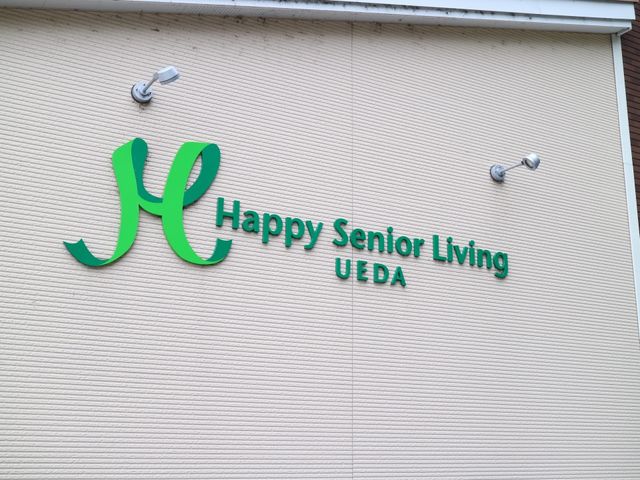 幸せを感じさせる看板 外壁 笑顔あふれる環境でお仕事しませんか。こちらは安心と信頼を象徴する名称を掲げた施設です。