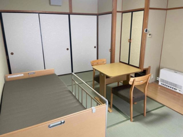 落ち着いた和室の居室 居室 畳の部屋で、温かみある和の雰囲気が心地よい居住空間です。ベッドとテーブルが配置されています。