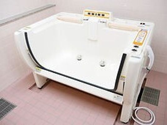 ピンクのタイルが敷かれた浴室に置かれた機械浴。浴槽の壁の一部が上下にスライドするデザイン。