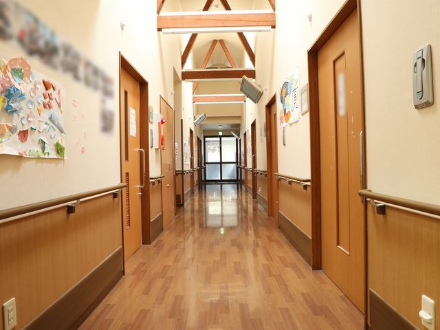 廊下の木目調デザイン 通路 木目調の床が温もりを感じさせる廊下です。壁には明るい色彩のアートが飾られ、安らげる空間が広がっています。