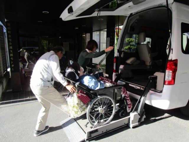 車椅子の乗降風景 エントランス 介護スタッフが丁寧に車椅子の利用者をサポートしています。介護の現場を直に感じられます。