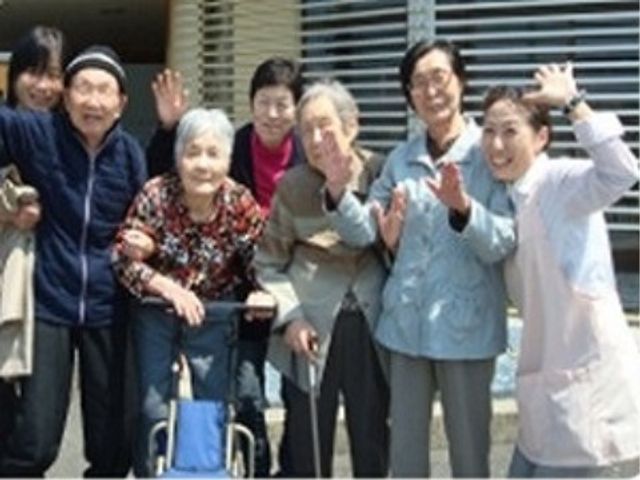 笑顔の集合 入居者様 元気な笑顔で手を振るスタッフと利用者の方々が印象的な光景です。あたたかい雰囲気の中での仕事をご希望なら、是非ご検討ください。