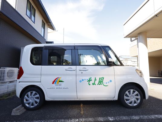 施設の写真 白い車体に緑の文字で施設名が記載された送迎車