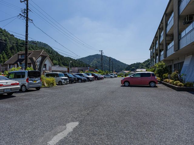 駐車場と建物外観 外観   建物前に広い駐車スペースがあり、車での来訪もしやすそうです。周囲には緑の山並みが見え、落ち着いた環境です。