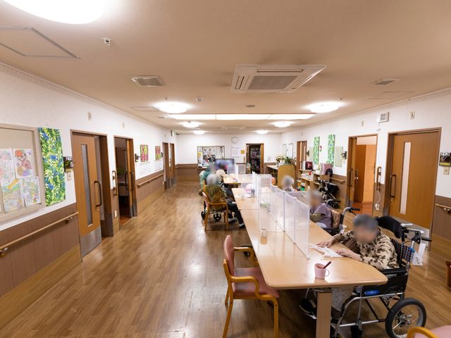 居室の廊下と居住者 共有スペース 廊下はゆったりとしており、壁にはカラフルな絵が飾られています。居住者の方々は自分のペースで快適に過ごしています。