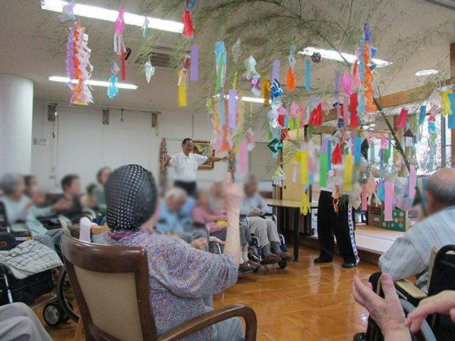 七夕飾りを楽しむ施設 リビング たくさんの七夕飾りが飾られ、明るくにぎやかな雰囲気です。利用者の皆さんが笑顔で和やかに過ごしています。