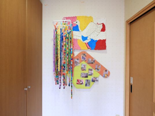 施設の写真 玄関を入った正面の壁に、鮮やかな折り紙で作られた千羽鶴と絵が飾られている。色紙の台紙には入居者様のお写真が貼られている。