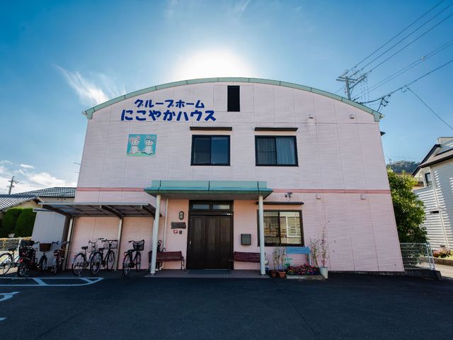 ピンクの外壁の建物 外観 暖かみのあるピンク色の外壁が特徴的な、心地よい印象を与える環境です。明るく清潔感のあふれる入り口がお出迎えします。