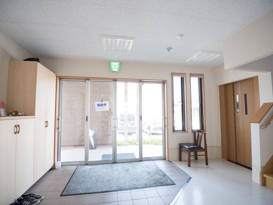 玄関は広々としており、バリアフリーとなっている。靴箱が置かれた正面には、エレベーターと階段がある。椅子も置かれている。