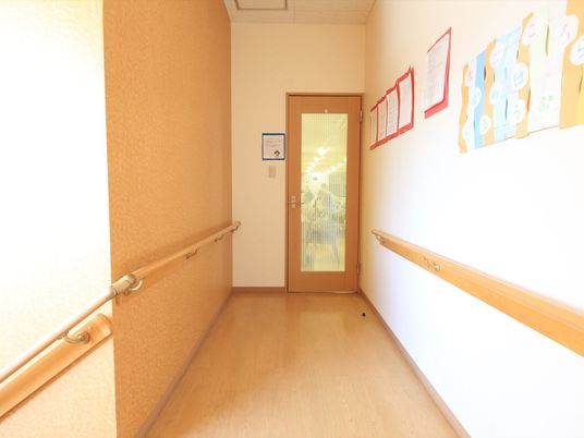 施設の写真 階段を上るとすぐに通路がある。通路の両側には手すりがある。壁には掲示物があり、進むと部屋の扉が見える。