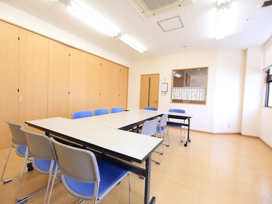 ライトブラウンの床と同系色の備え付けの棚が並んでいる広い部屋がある。会議用のテーブルと椅子が置かれ、たくさんの人が座れるようになっている。
