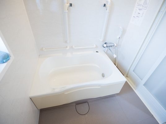 浴室内の壁と浴槽は白色で、床はグレー色である。壁には縦と横の手すりが複数備えられている。シャワーや水道の蛇口もある。