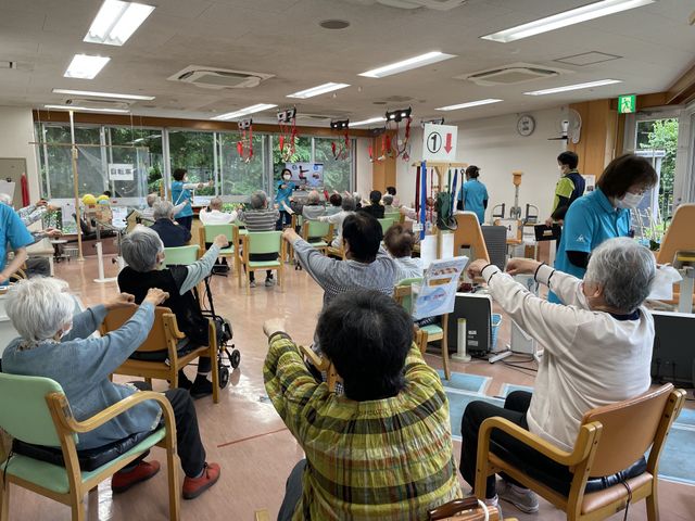 活動的な機能訓練室 機能訓練室 ゆったりと座れる椅子に座った多くの方々が、指導員のもとリハビリテーションに取り組んでいます。