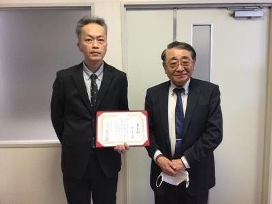 表彰状を持つ男性2人の室内  