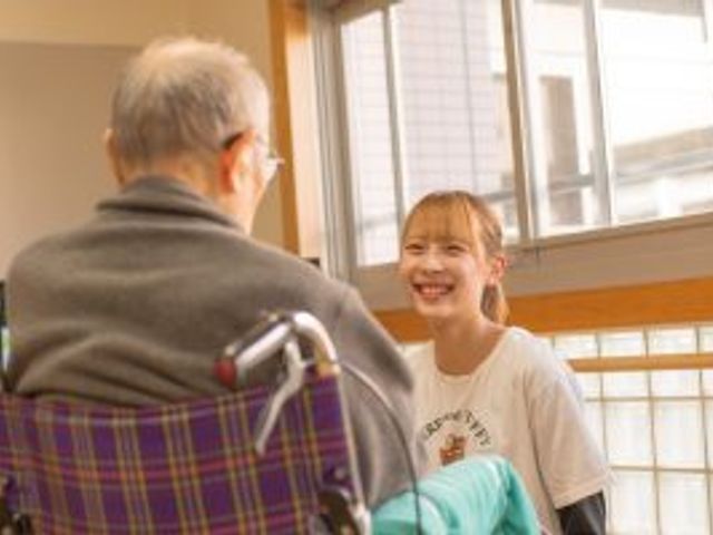 笑顔溢れるコミュニケーション スタッフイメージ 穏やかな表情のスタッフが、ご利用者様と温かい対話を楽しんでいます。明るい窓辺でのひと時です。
