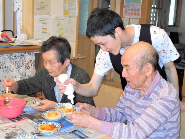 スタッフ介助の食事風景 ケーキ作り スタッフが優しく介助する温かい食事の時間です。共に食べ、笑顔が溢れる空間がここにあります。