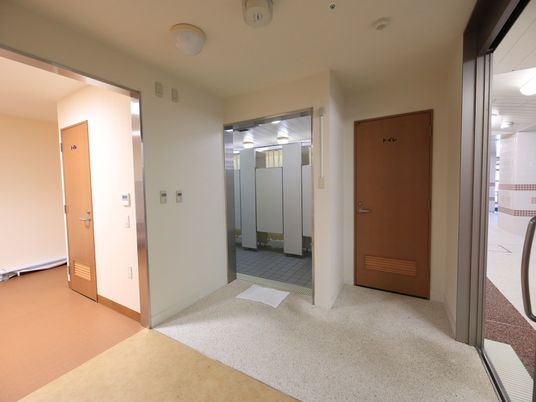 タイル敷きのスペースがあり、その奥は個室ごとに区切られている。右側にトイレのドアがある。右の壁にガラスの引き戸が設置されている。