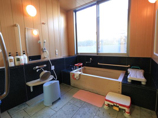 床に石材を使用した浴室で、浴槽はヒノキでできている。浴槽周囲に手すりや滑り止めマット、腰掛けが置かれている。左側に洗い場がある。