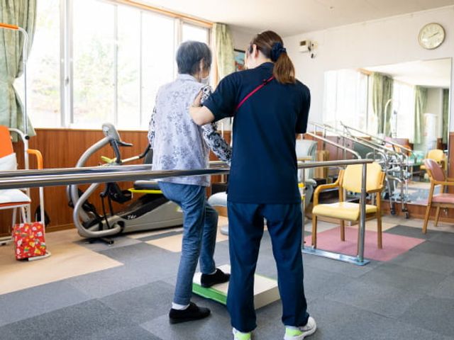 支援を受ける利用者とスタッフの機能訓練室 機能訓練室 自然光が差し込む訓練室で、利用者とスタッフが一緒にトレーニングに取り組んでいる様子です。