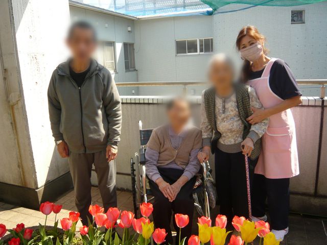 チューリップと人々の中庭 中庭 色とりどりのチューリップが咲く中庭で、利用者とスタッフが心地よく過ごしています。