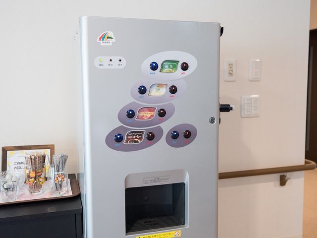 自動販売機と小物置き台 給茶機 スタッフや利用者がリフレッシュできる自動販売機が設置されていて、お茶やコーヒーを手軽に楽しめる環境が整っています。