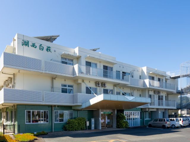 車が停まる建物外観 外観 駐車スペースが充実した、清潔でモダンな建物です。青空が広がる環境が魅力です。
