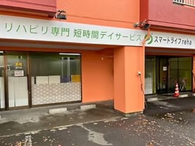 リハビリ専門の外観 外観   オレンジ色の外壁が印象的な、リハビリ専門の事業所です。建物前には出入りしやすい広めの通路が見えます。