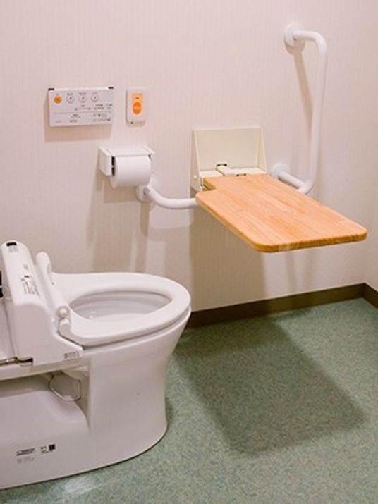 ふたのないトイレが設置され、広さも十分あり、可動式の木製の台が便器の前に設置されている。