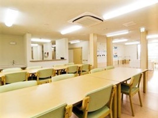 木製の長いテーブルと椅子が複数並んでいる施設内の共有スペース。食堂のような雰囲気の場所