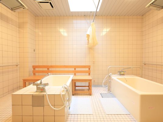 浴室に２つの浴槽が設置されている。それぞれの浴槽の脇には白色の滑り止めマットが敷かれ、間にはカーテンがある。