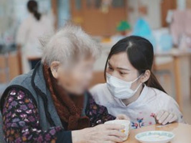 共同スペースでの交流 ラウンジ 広々としたラウンジで、スタッフが優しく利用者と寄り添っています。温かい雰囲気が感じられます。