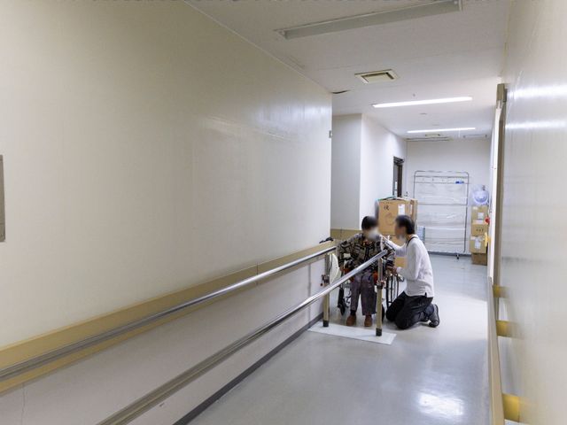 手すり付き廊下と人物 廊下 白く清潔感のある廊下で、丁寧に支援するスタッフの様子が伝わります。