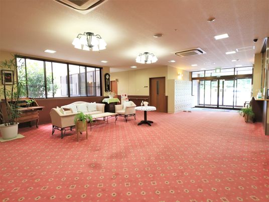 玄関ホールには、赤地のカーペットが敷かれている。観葉植物や調度品のそばに、ソファやローテーブルが置かれている。