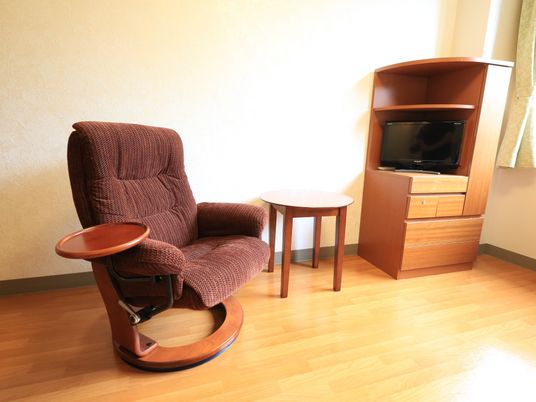 居室に、丸いサイドテーブルのついたソファチェアが置かれている。窓際の収納家具にテレビが収まっている。