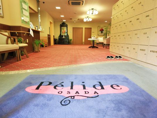 玄関に、施設名称が織り込まれたカラフルな足ふきマットが敷かれている。右側に設置された靴棚の扉に、居室番号が書かれている。